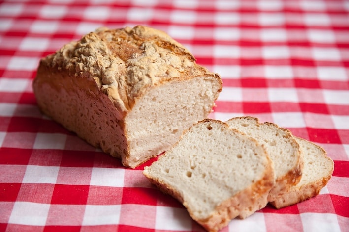 The original photo of a sliced loaf of bread srsly bread on a red and white checkered tablecloth.