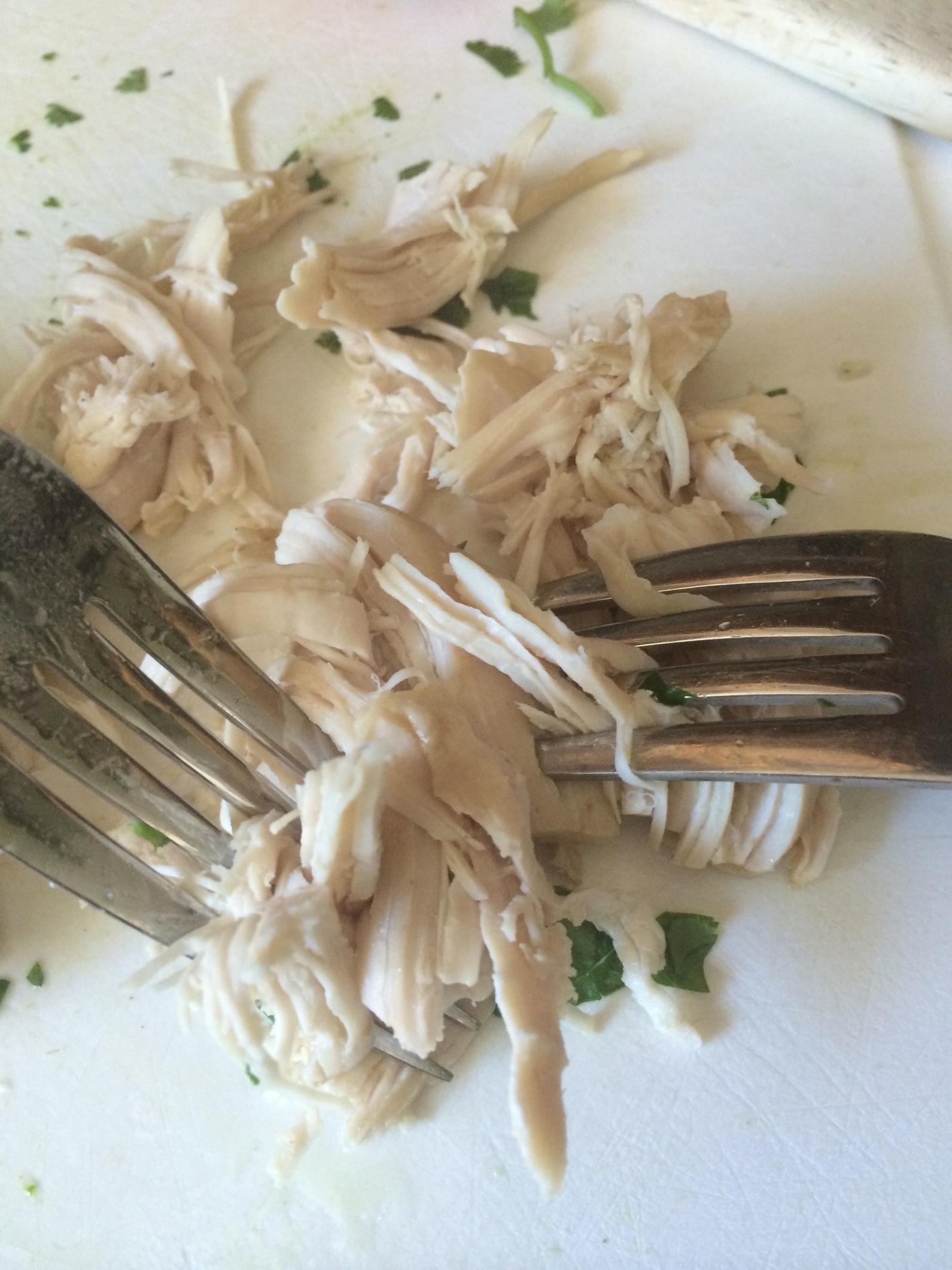 Shredding chicken with two forks on a cutting board.