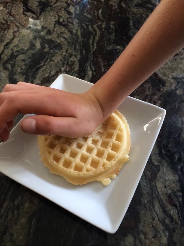 Flattening a gluten free waffle with the palm of a hand to create a gluten free ice cream cone.