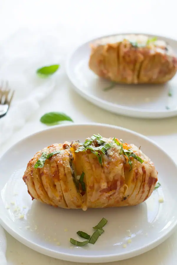 Easy hassleback potato recipe stuffed with pizza toppings and served on white plates.