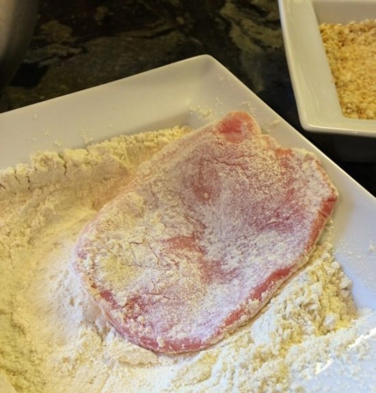 A photo showing the dipping a pork cutlet in flour.