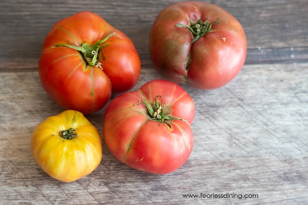 Four large heirloom tomatoes on a wooden table.