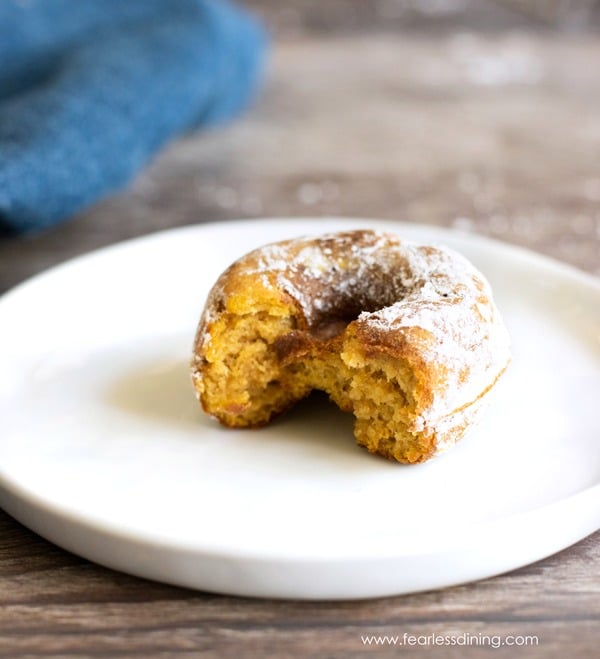 A gluten free pumpkin donut on a plate. A bite has been taken out of the mini donut.