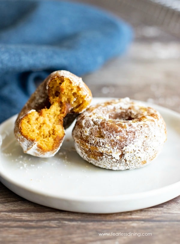 Two gluten free pumpkin donuts on a plate. One mini donut has a bite taken out