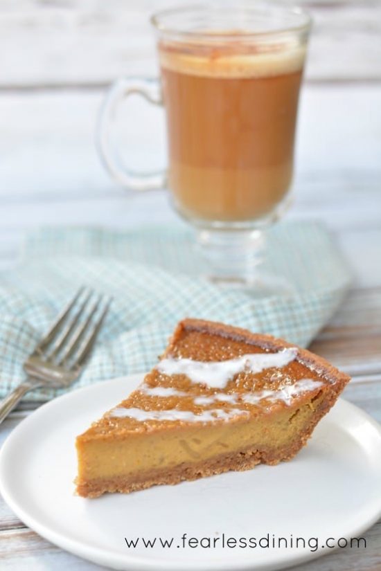 A slice of Gluten Free Sweet Potato Pie on a plate. A latte in a glass mug is behind the plate