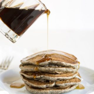 maple syrup being poured onto a stack of gluten free buckwheat pancakes