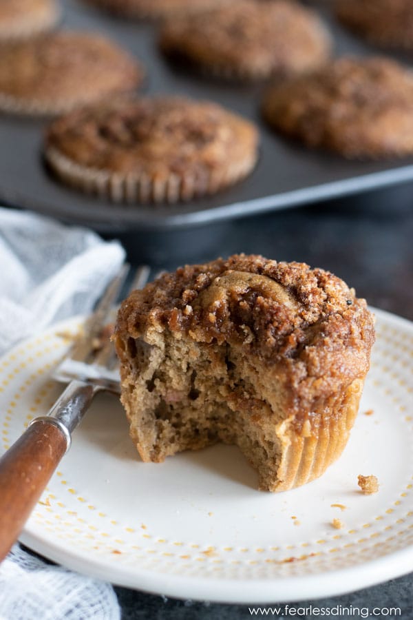 A gluten free cinnamon streusel muffin on a plate with a bite taken out.