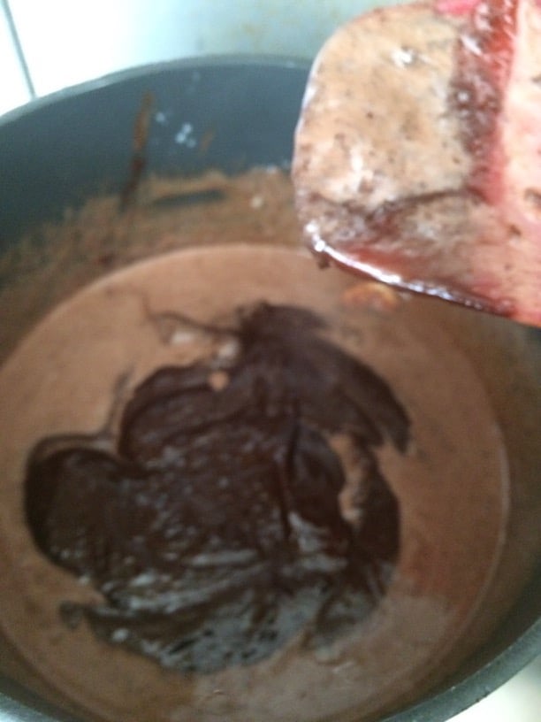 The melting chocolate in a pot getting stirred.