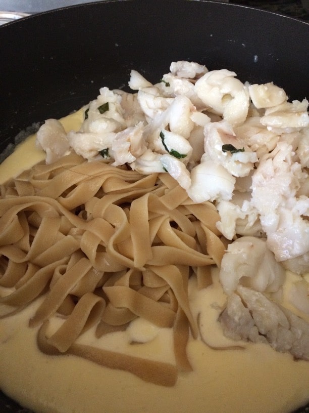 Mixing cooked pasta and cod into the alfredo sauce