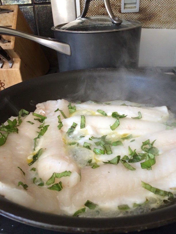 Filets of cod with fresh basil cooking in a skillet.