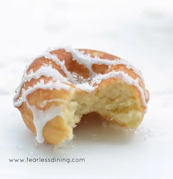 A single Gluten Free Lemon Donut with a bite taken out so you can see how light and fluffy the inside is.
