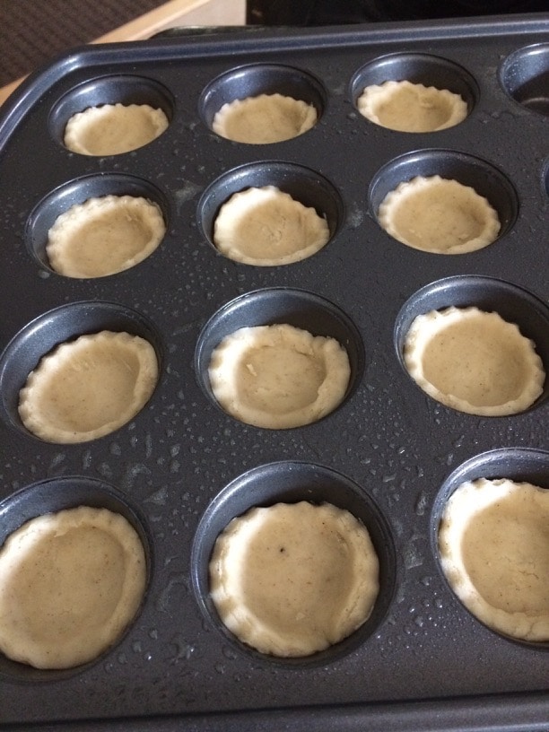 A mini muffin tray with the cannoli dough in each section.