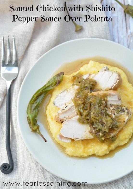 Chicken with Shishito Pepper Sauce Over Polenta on a plate. A fork is next to the plate. A roasted shishito pepper is on the side of the plate