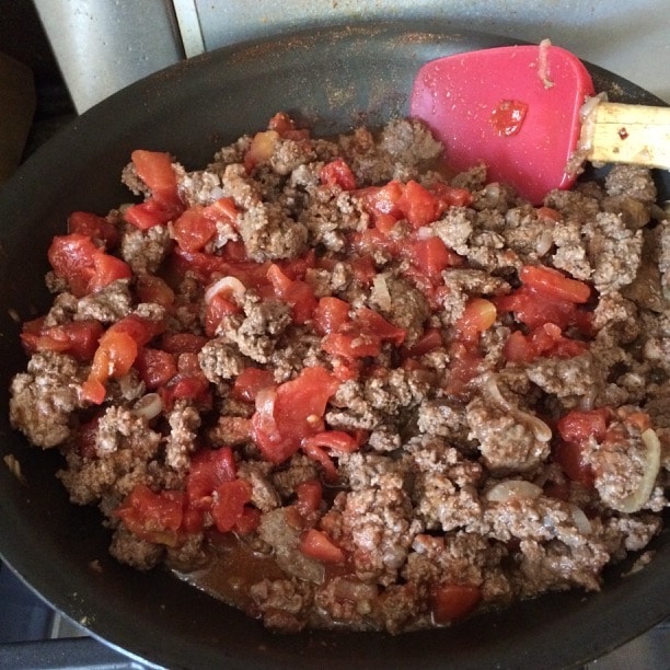 The cooked ground beef with tomatoes and seasoning in a skillet.