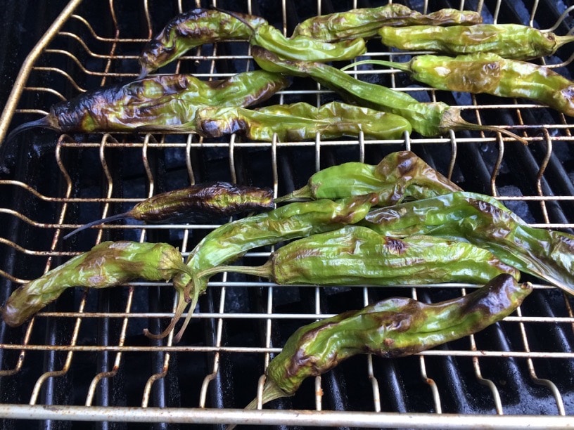 Shishito peppers roasting in a grill rack.