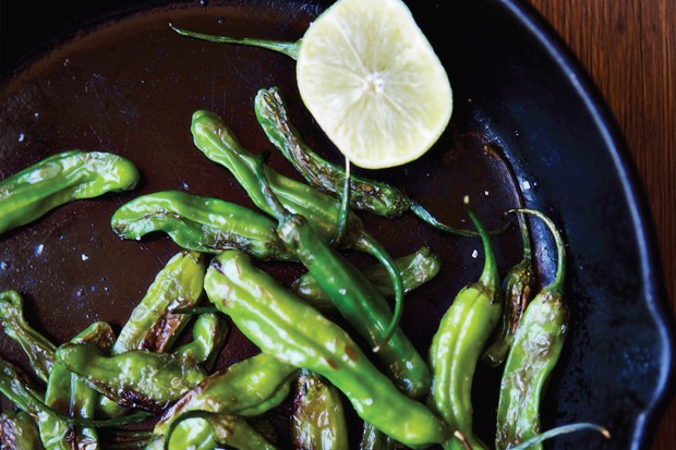 Shishito peppers roasting in a cast iron pan.