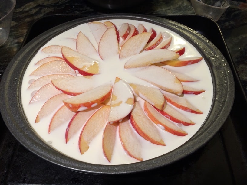 The apple cake batter in the pan with the sliced apples on top.