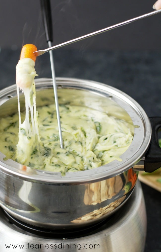 Gluten Free Spinach and Leek Cheese Fondue with a carrot dipped into the hot cheese 