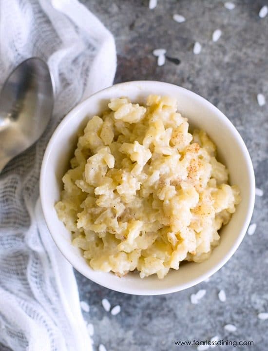 A top view of a white bowl of rice pudding. A spoon is next to the bowl.