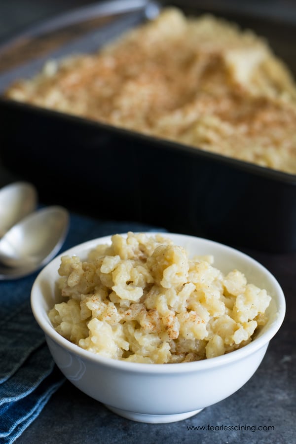 A white bowl filled with rice pudding. The pan of rice pudding is behind the bowl.