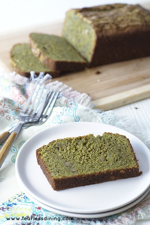 A slice of Gluten Free Matcha Green Tea banana bread on a plate with the bread loaf in the background.