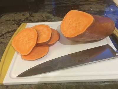Slicing a sweet potato on a cutting board.