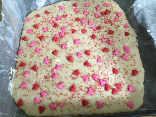 Cooling chocolate in a pan. The top of the melted chocolate is covered in heart sprinkles.