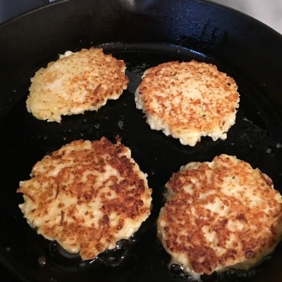 Frying cheesy gluten free cauliflower pancakes in a cast iron skillet.