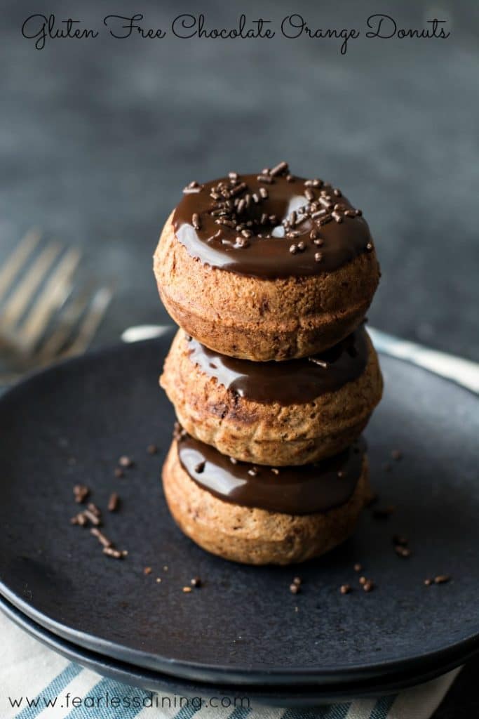 A stack of three Gluten Free Chocolate Orange Donuts on a black plate.