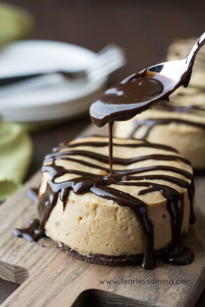 Drizzling hot chocolate fudge on top of Gluten Free Peanut Butter Chocolate Mini Cheesecakes.