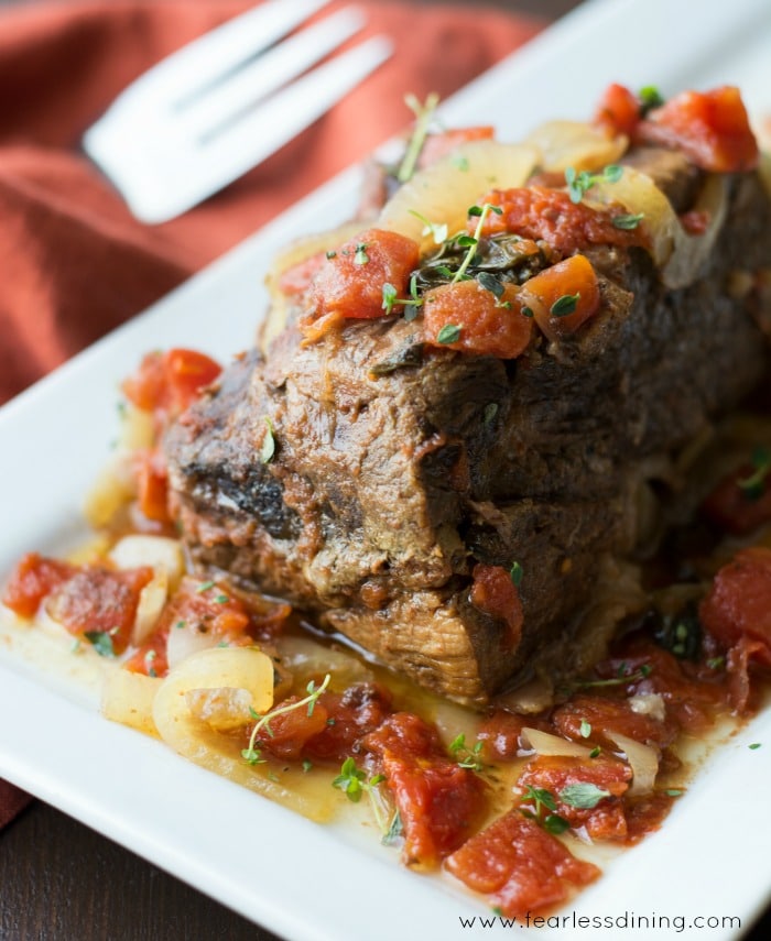 Moist and Juicy 5 Ingredient Crockpot Roast from the side view surrounded by onion and tomatoes.
