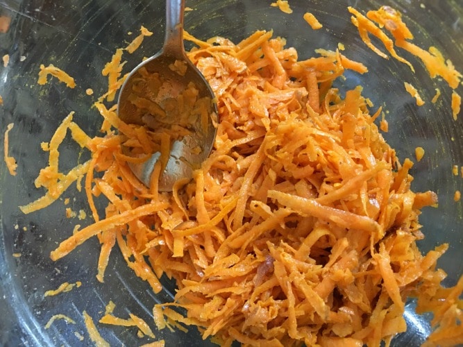 combining grated sweet potato and curry powder in a bowl.