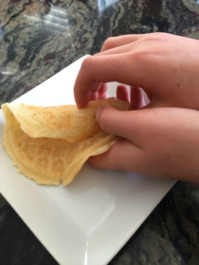 Rolling a gluten free waffle closed to become a gluten free waffle cone.