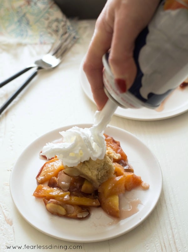 Putting whipped cream onto the peach cobbler.
