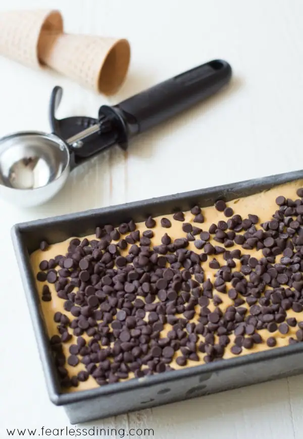 No-Churn Caramel Chip Ice Cream frozen into a loaf pan, with an ice cream scoop and cones next to it.