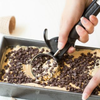 Someone removing a scoop of chocolate chip caramel ice cream from a container