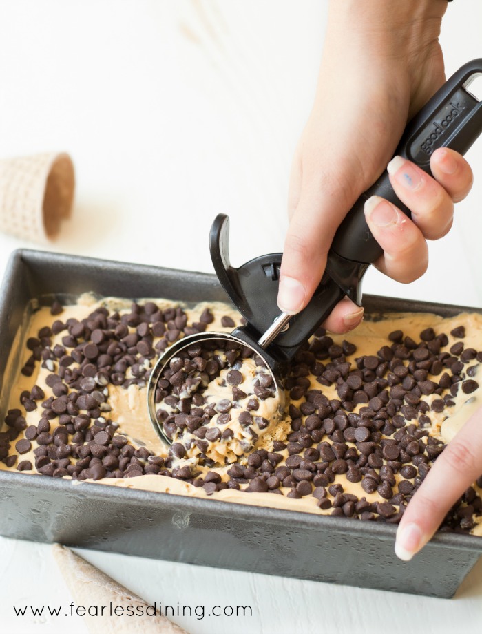 Someone removing a scoop of chocolate chip caramel ice cream from a container