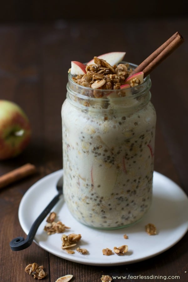 Easy Apple Crisp Overnight Oats in a mason jar. The jar is on a white plate with an apple in the background.