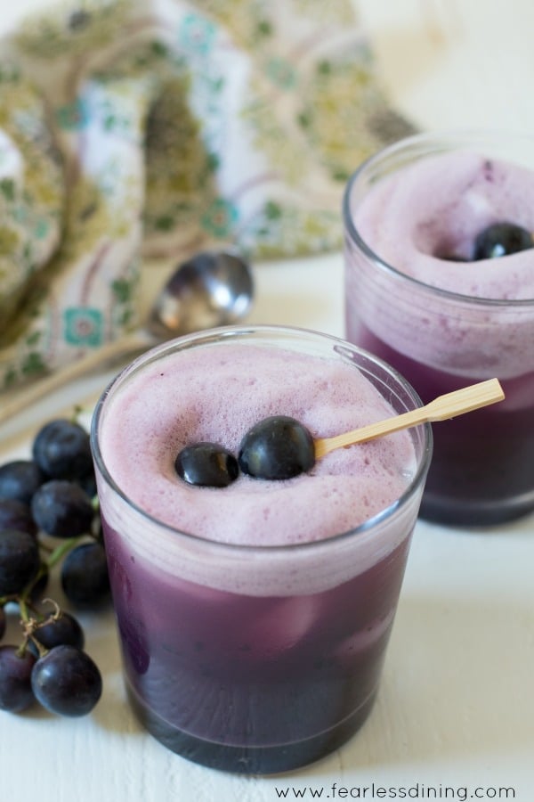 Two glasses of grape burbon cocktails. They are garnished with black grapes on a toothpick.