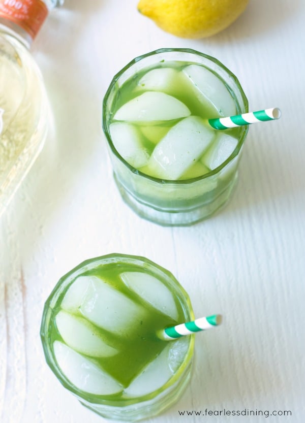 Top view of two glasses of lemonade and tequila cocktails. Ice cubes and a green and white striped straw are in the glasses.