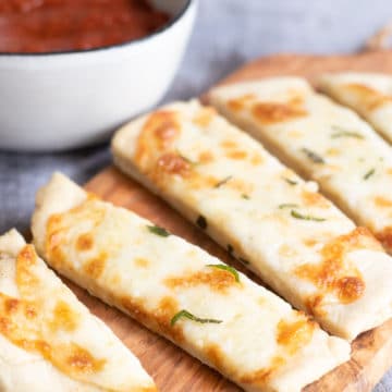 A cheese topped sliced gluten free flatbread on a wooden cutting board.