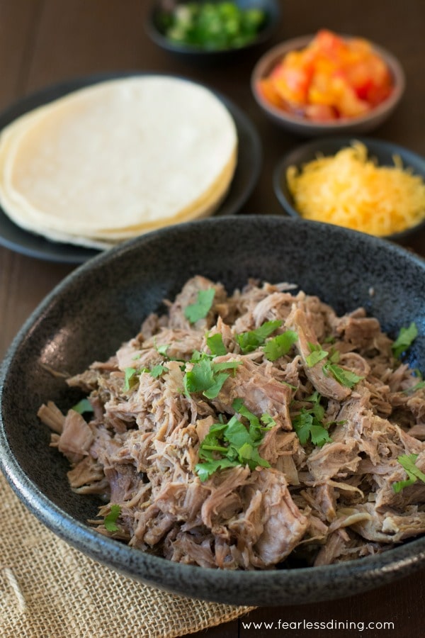 Easy 5 Ingredient Slow Cooker Pulled Pork in a bowl with tortillas and taco in the background.