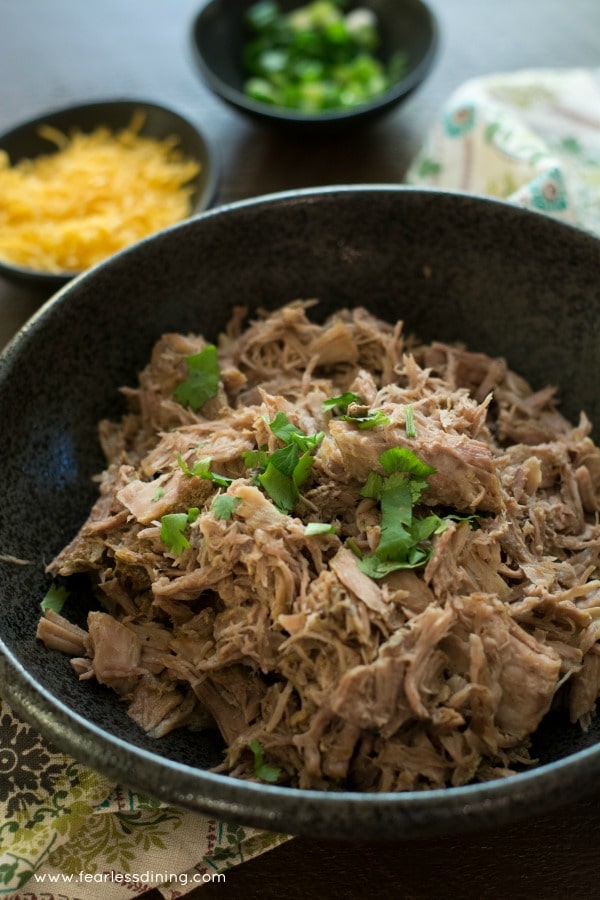A large black bowl of pulled pork with shredded cheese in the background