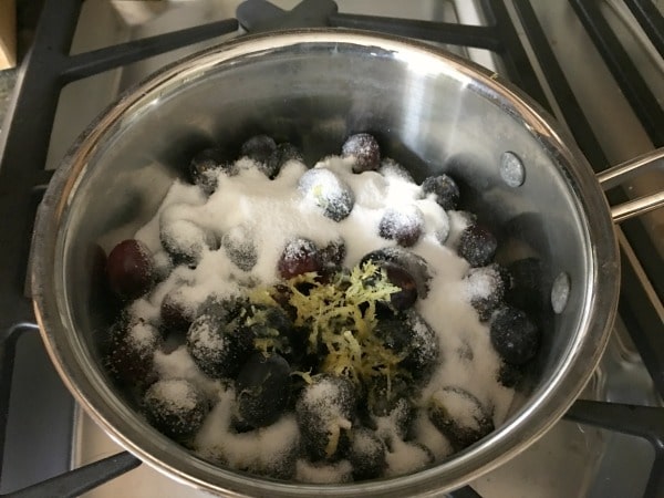 Cooking black grapes with sugar and lemon zest in a pan.