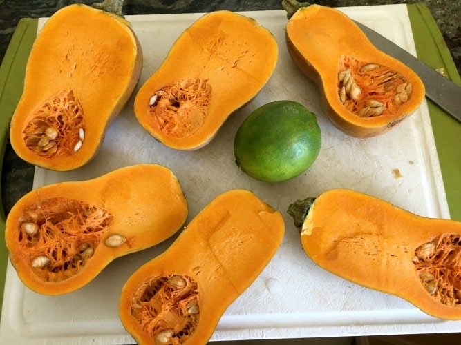Halved honeynut squash on a cutting board next to a lime.