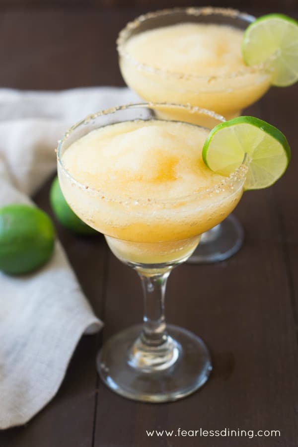 Two glasses of frozen peach margaritas with a lime garnish.