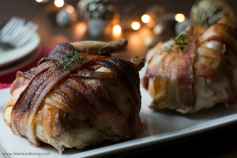 Bacon wrapped cornish game hens with plates in the background.