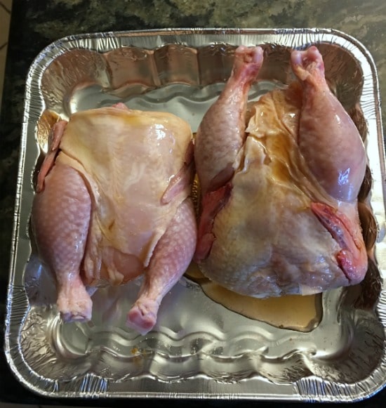 Two cornish game hens in a baking tin with maple syrup