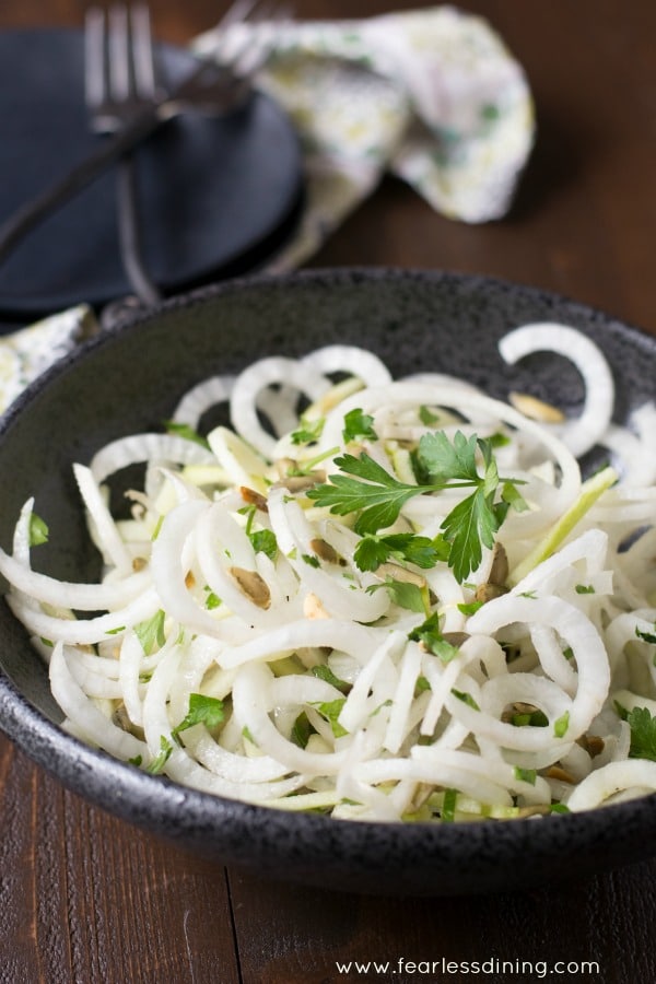 Daikon and Green Apple Salad with Pepitas in a black bowl. Plates and forks are in the background