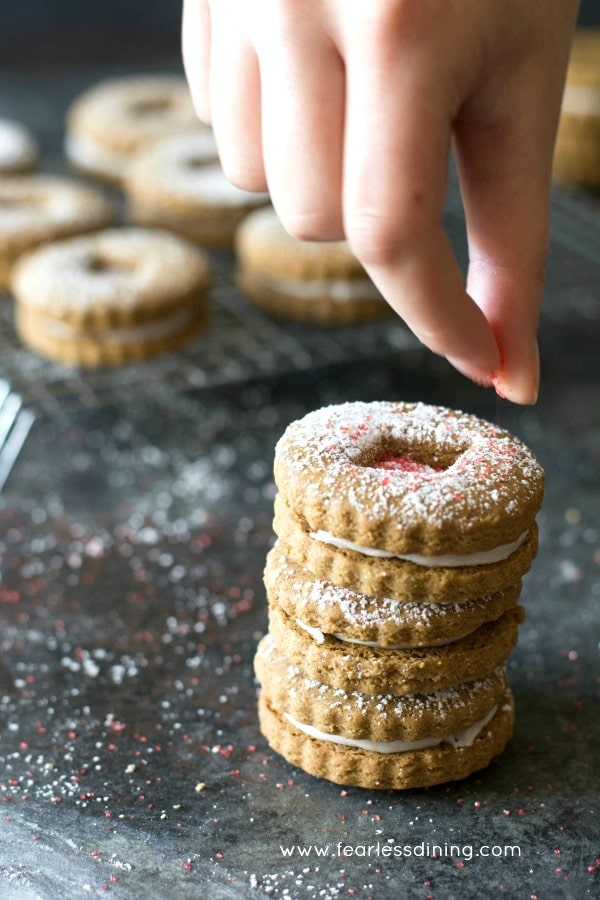 Adding red sprinkles to gluten free gingerbread linzer cookies.